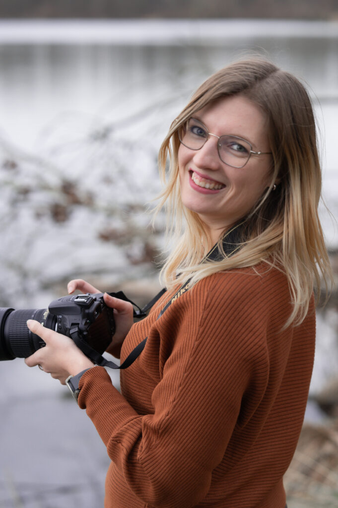 Fotografin Caroline Nagl (Carografie) mit Kamera und Lächeln bei der Arbeit in Linz am Weikerlsee